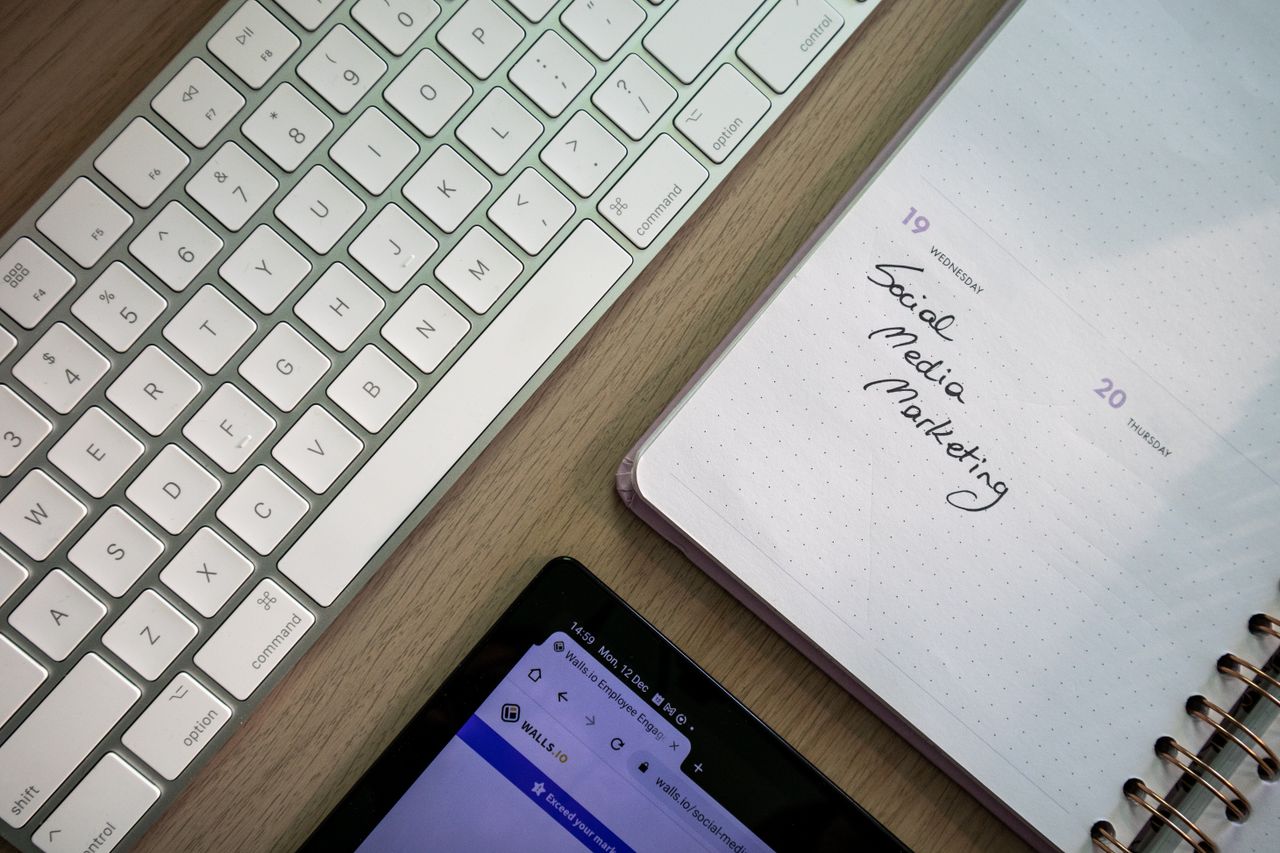 who-we-are Top view of keyboard, planner with social media marketing note, and tablet on a desk.